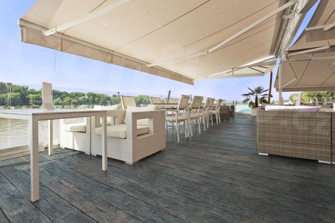 Velká terasa restaurace s podlahou Millboard Embered ve stínu pod markýzami.